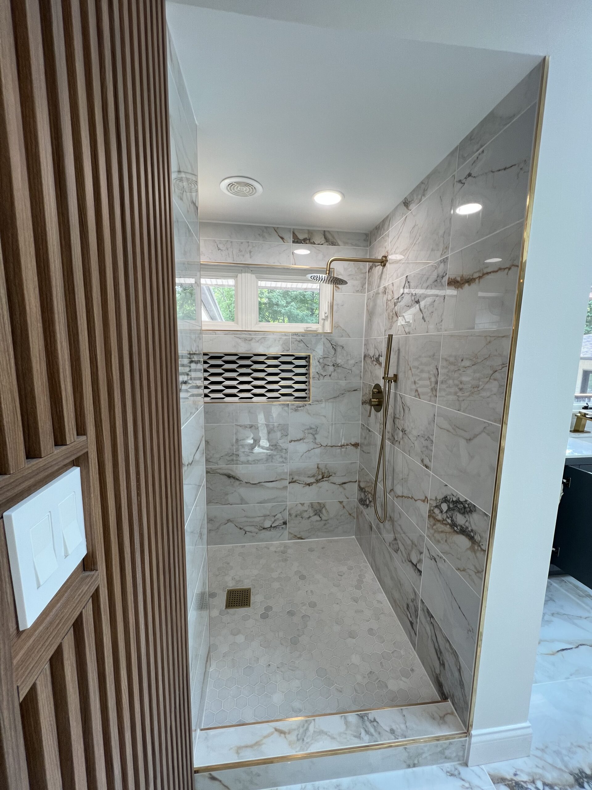 Residential shower, black and white tile, marble tile, with rainfall showerhead. From a view that shows shelf space