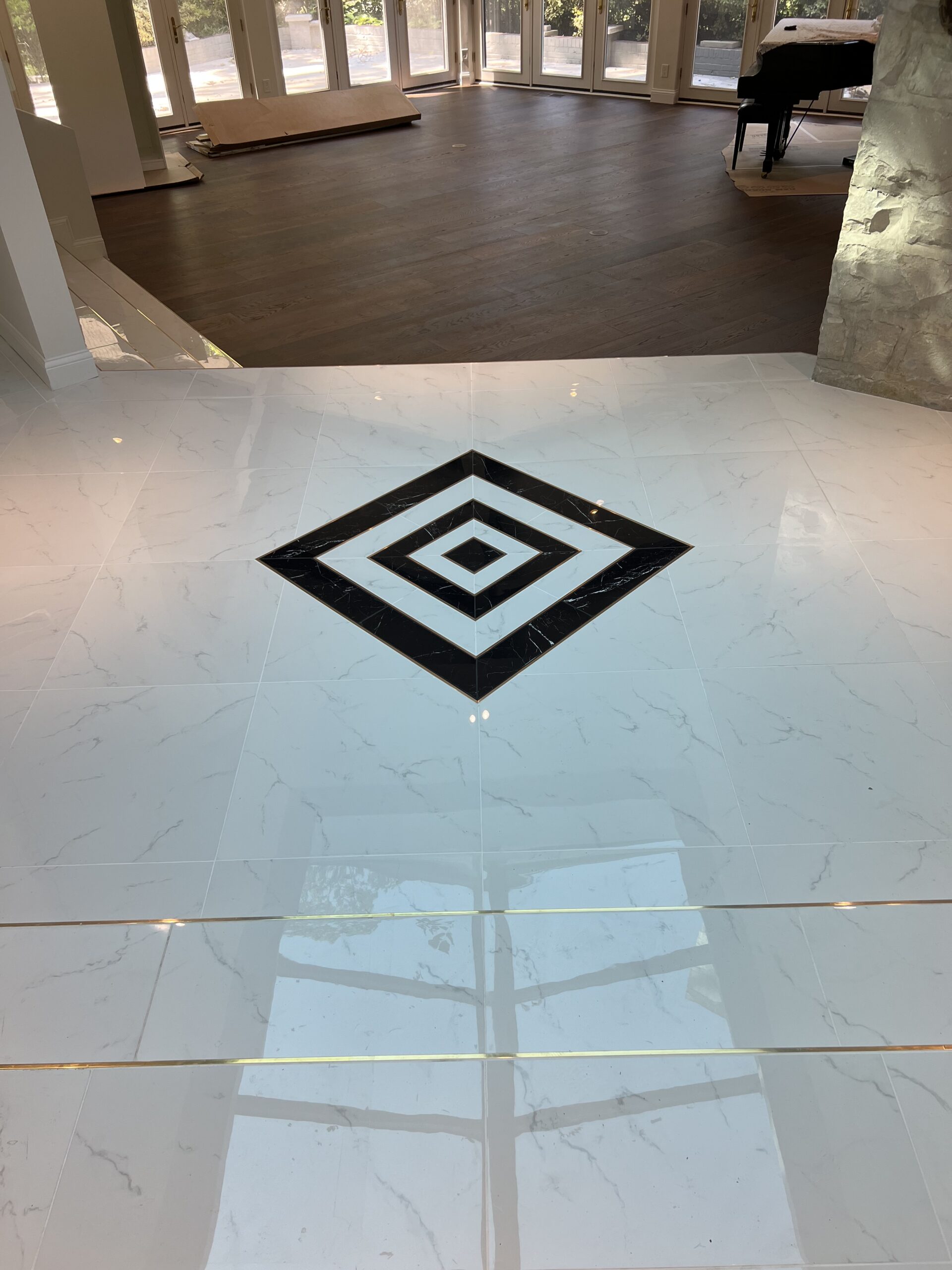 Different view of black and white tiles arranged in square pattern facing room with wooden floors and a grand piano